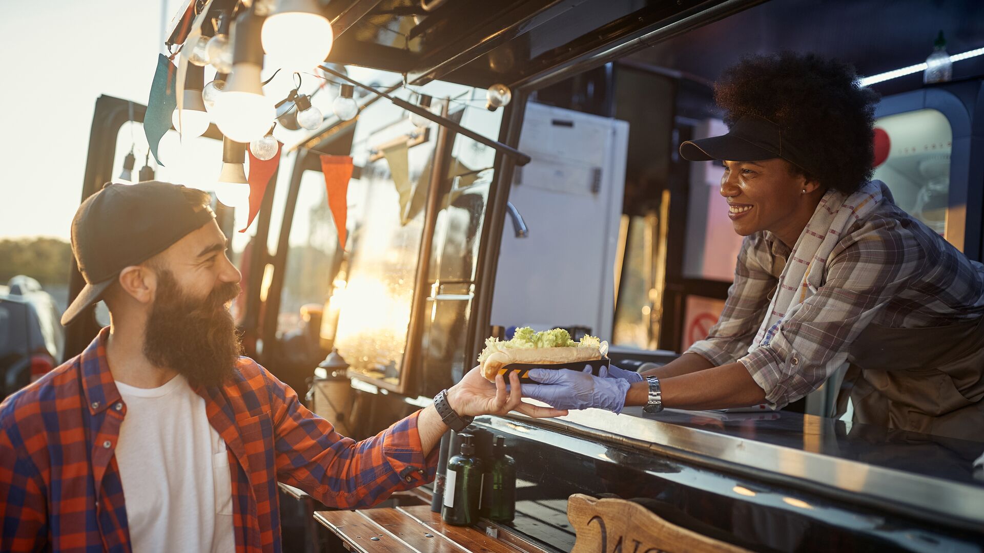 sprachaufenthalt-neuseeland-christchurch-little-high-eatery afro-american female employee gives with care and smile a sandwich to young hipster male customer