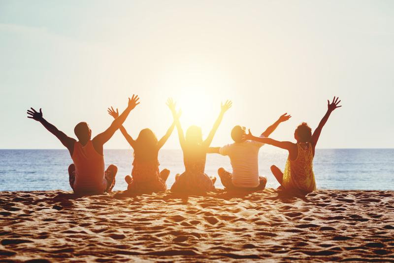 Group on Beach Group of five happy people sits on background of empty sunset beach. Travel or sea vacations concept